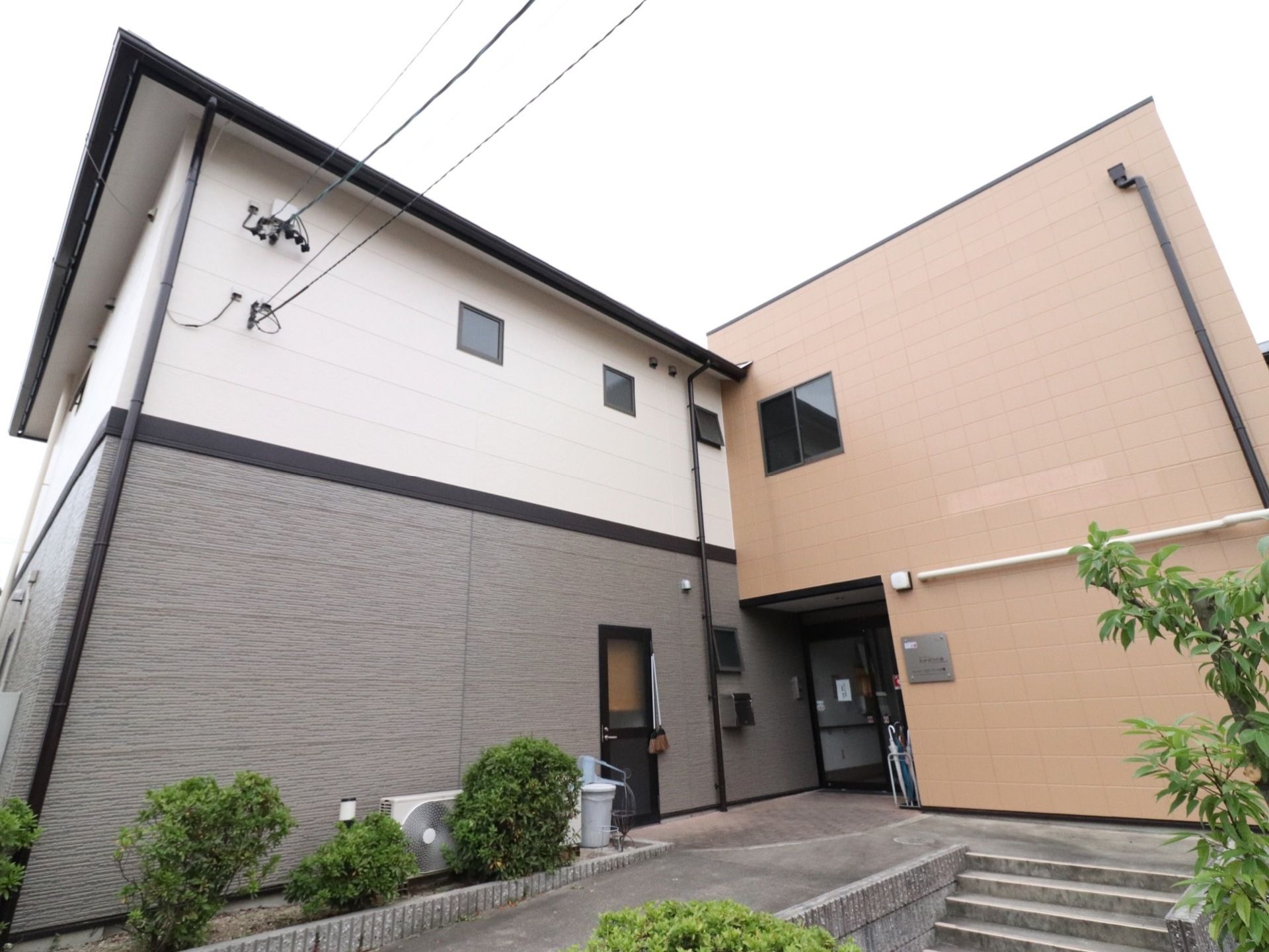 施設のエントランスである。スロープと階段が設けられている。玄関脇の外壁には施設名が記されたプレートが掲げられている。