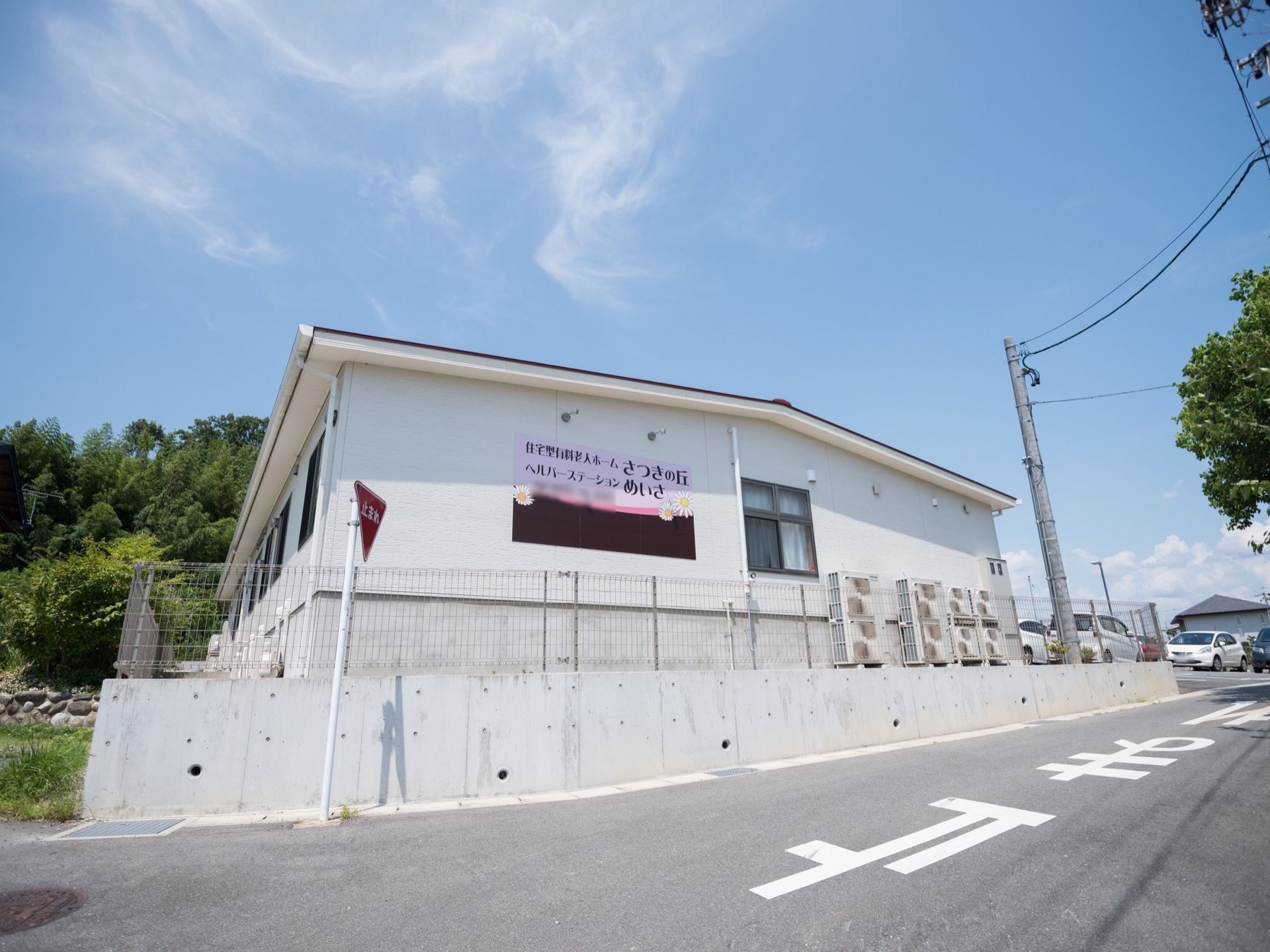 駐車場へと向かう道路側の壁に、薄いピンク色を用いた看板が付いており、ホーム名と併設施設名が書いてある。