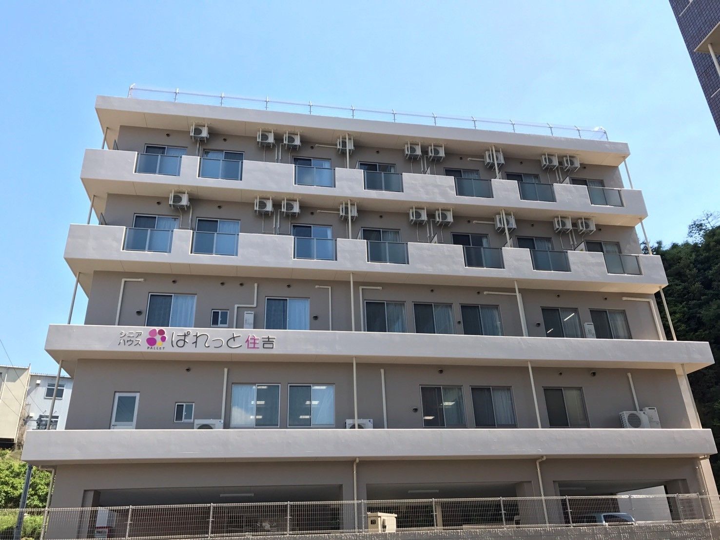 淡い色合いの外壁が落ち着いた雰囲気である。建物の１階には駐車場があり、４階と５階にはベランダが設置されている。