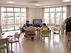 2面ある広い窓からは多くの光が差し込んでおり、明るい空間である。木製のテーブルや椅子が置かれており、入居者様同士で集まることができる。