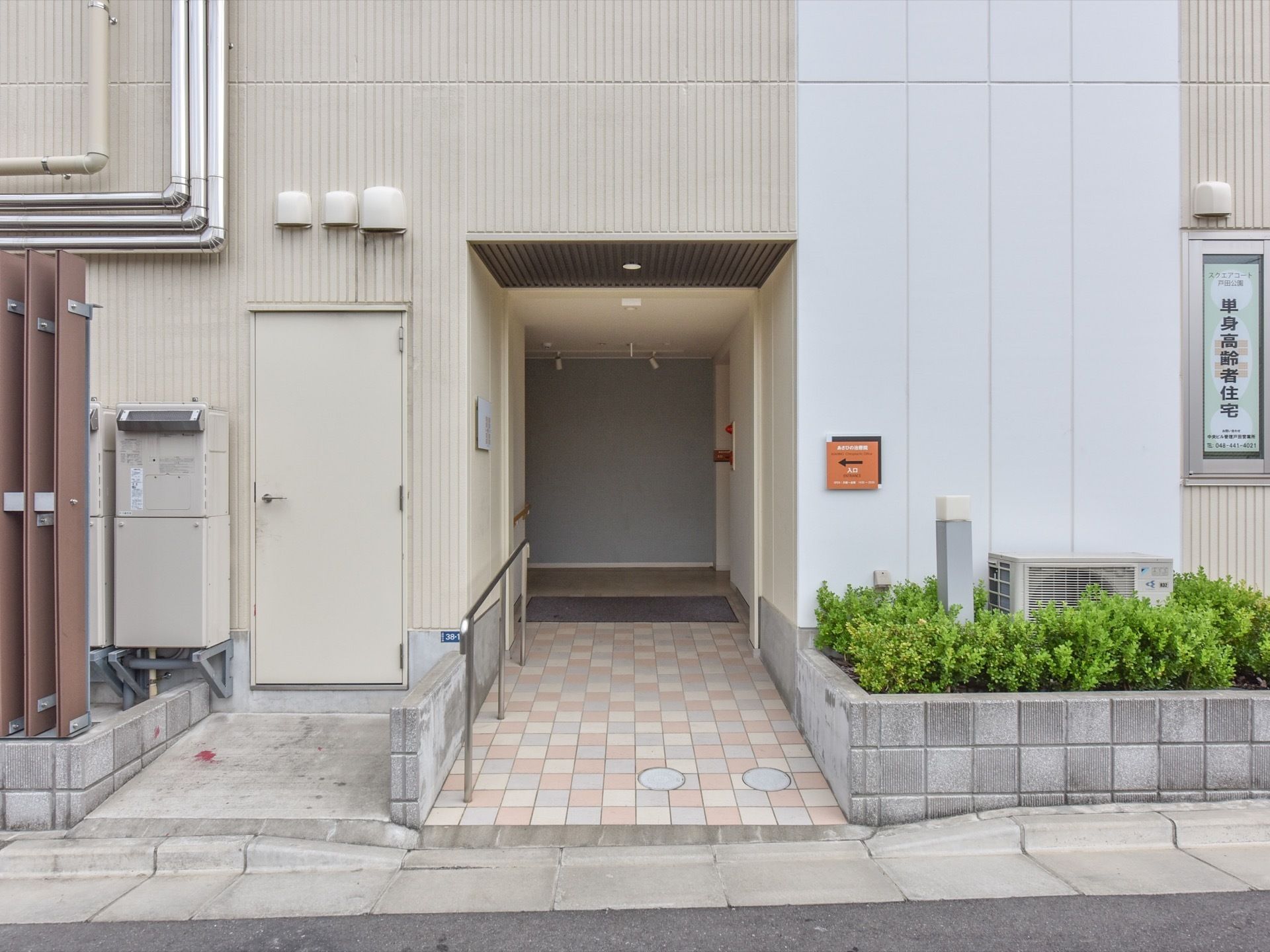 あさひの治療院の文字と矢印が書かれたプレートが建物の外観に取り付けられている。矢印がさす方向には入り口がある。