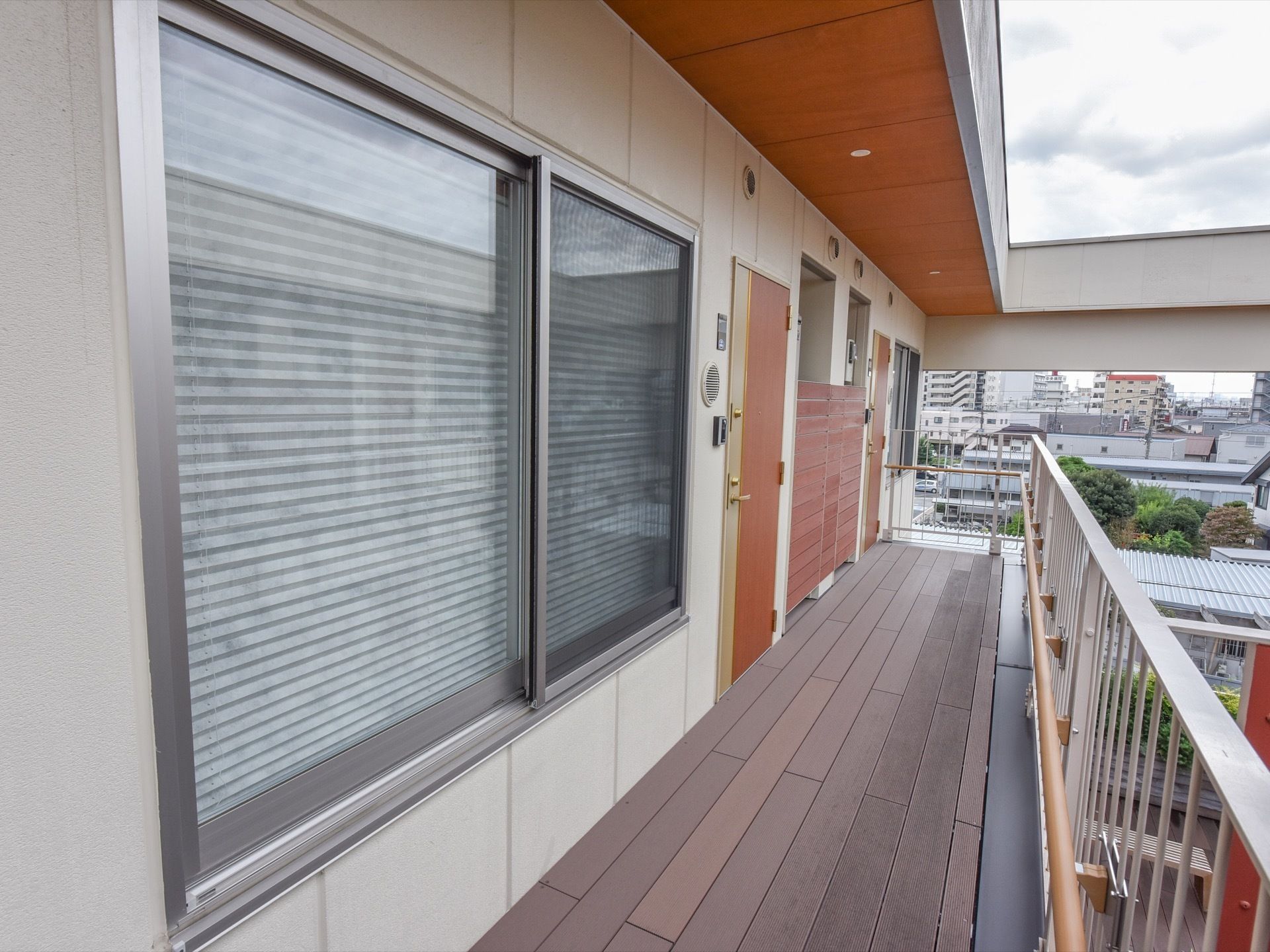 中庭の通路部分には入居者様の部屋がある。茶色い扉の横にはインターフォンが付いている。窓にはブラインドカーテンが掛かっている。