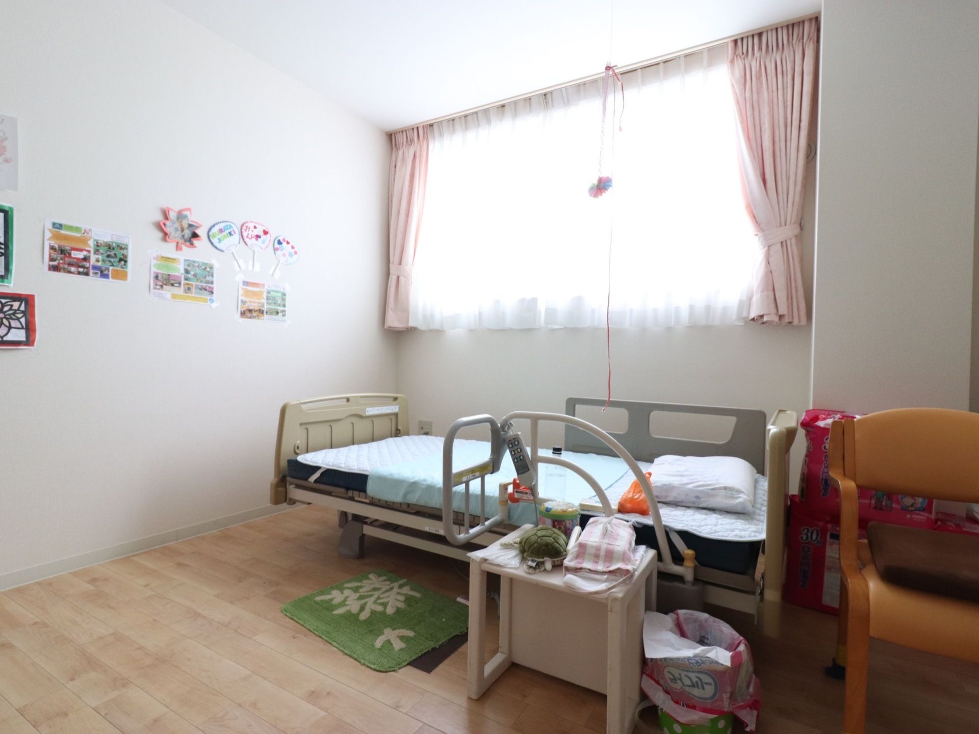 大きな窓のある明るい居室。リモコン操作する介護用ベッドが設置されています。天井から照明の長い紐が下がっている。