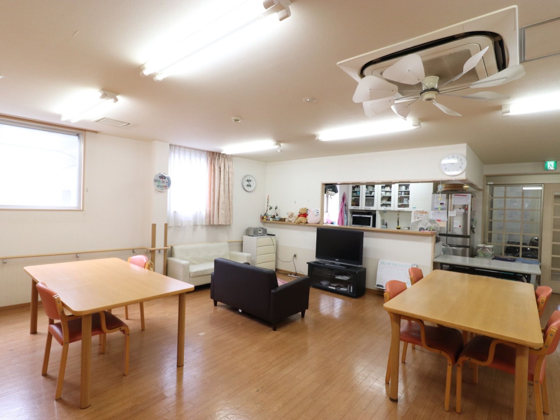 白色の天井と壁に木目の床である。天井にはエアコンを設置し、その上にファンを設けている。木製のテーブルと椅子、ソファなどを並べている。