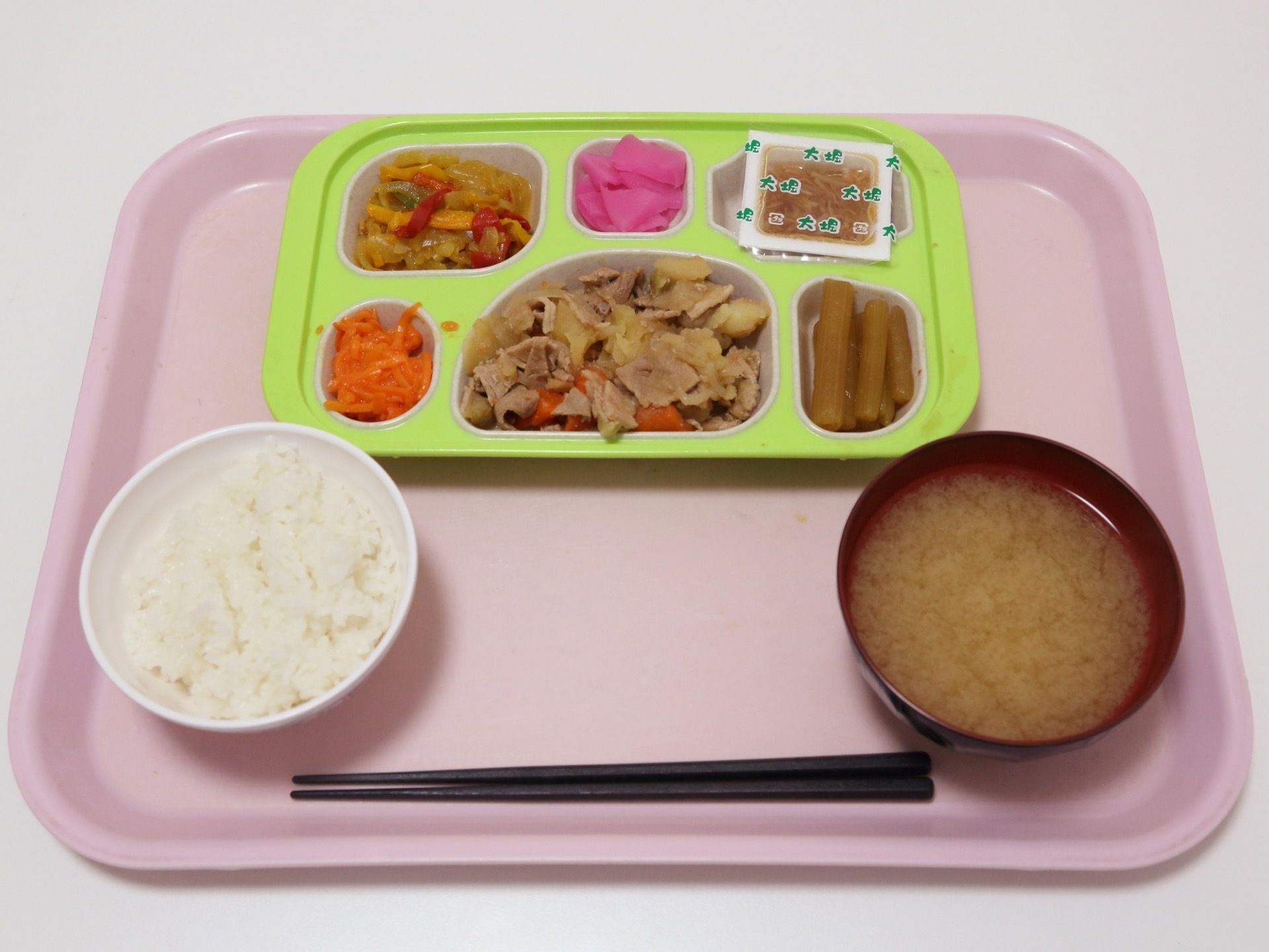 ピンクのトレイにご飯やみそ汁、数種類のおかずが入れられた仕切プレートが置かれている。箸も用意されている。