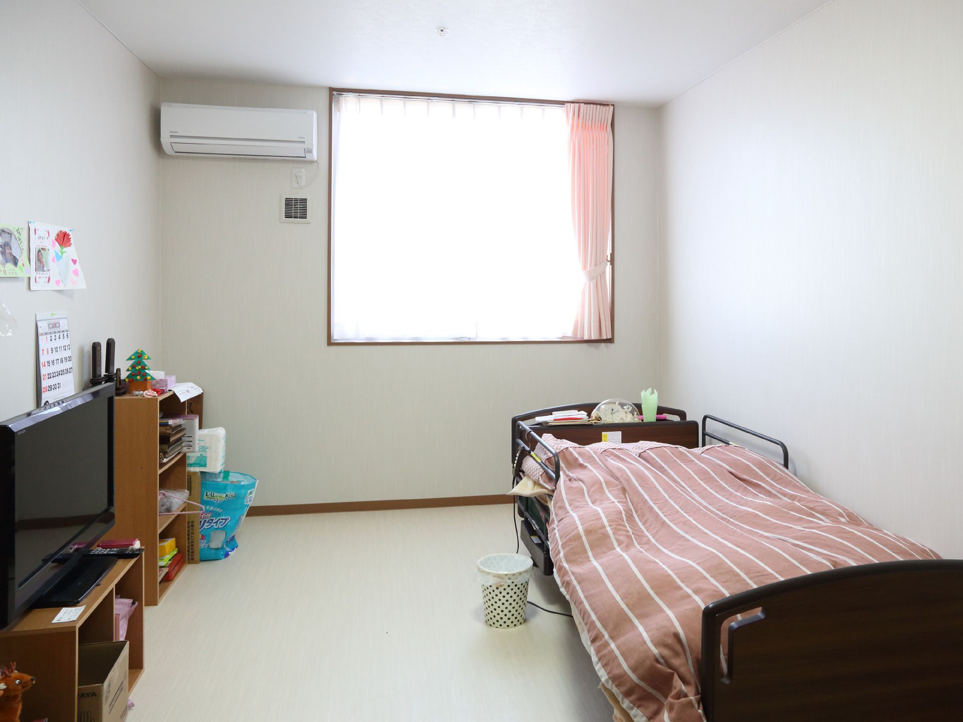 介護用ベッド、収納家具、テレビが置かれた、腰高窓のエアコン付き居室