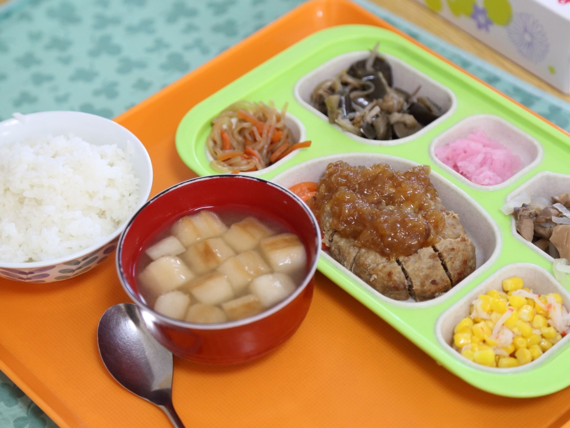当ホームで提供される食事の1例。ご飯や吸い物、豊富で色とりどりのおかずがお盆に載せられている。おかずはプレートに盛り付けられている。