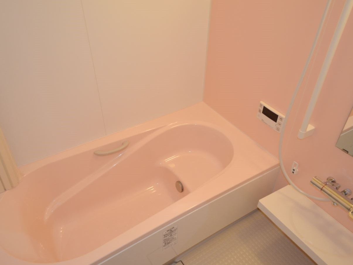 家庭サイズの湯船と壁が薄いピンク色になっていてやさしい雰囲気。湯船内に座れる部分もあり、ゆっくりと入浴を楽しめる。