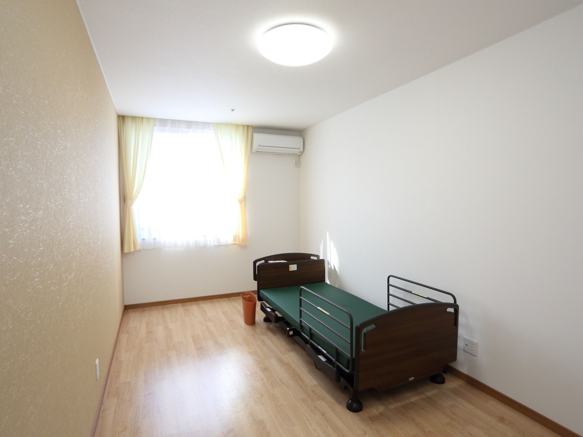 白を基調とした明るい居室には、介護用ベッド、LEDライト、エアコン、カーテンといった必要最低限のものが備わっている。