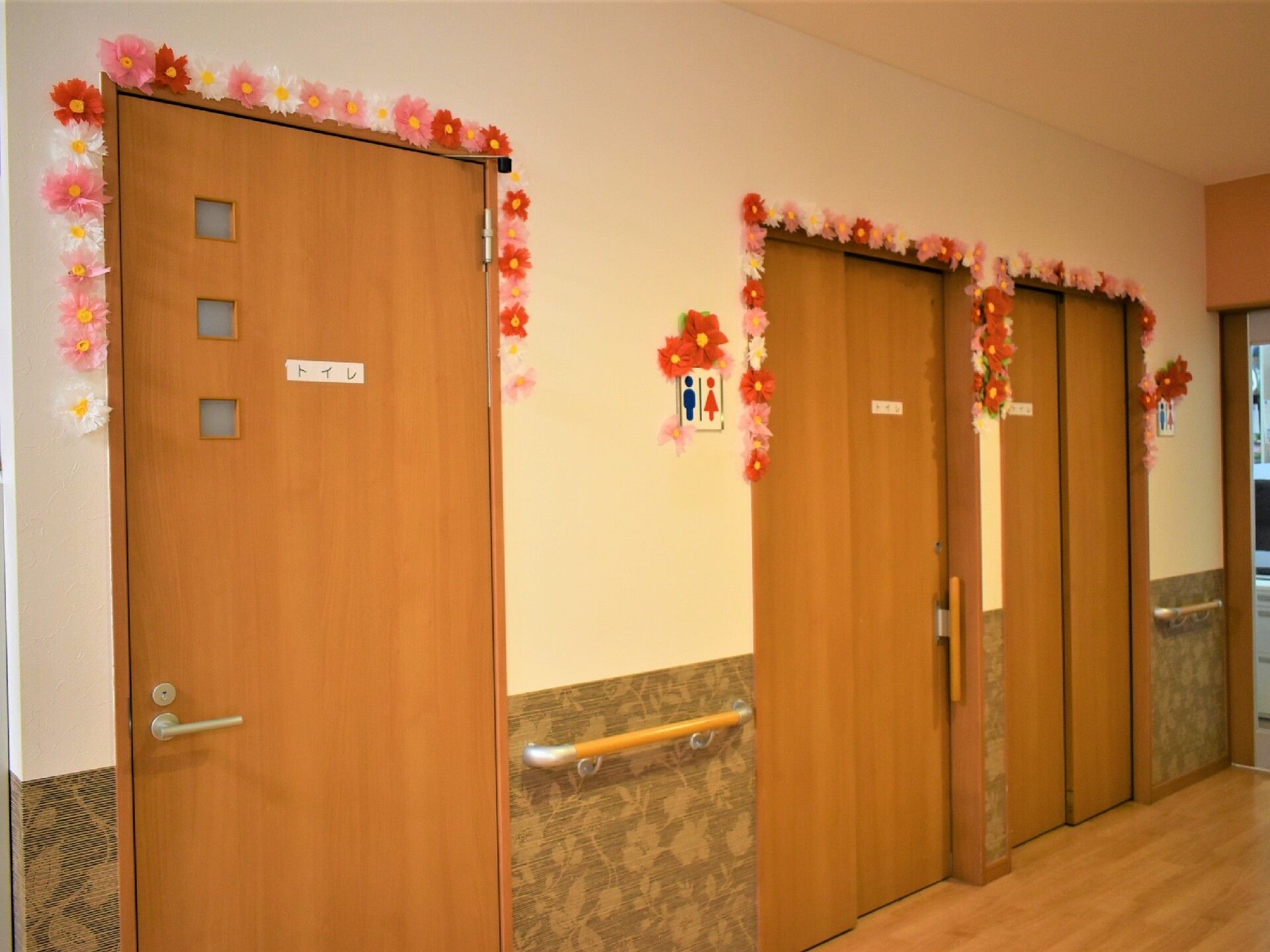 トイレには小さな窓が付いていてドアの回煮は手作りのピンクや白、赤い花が飾られている。壁には手すりも付いている。