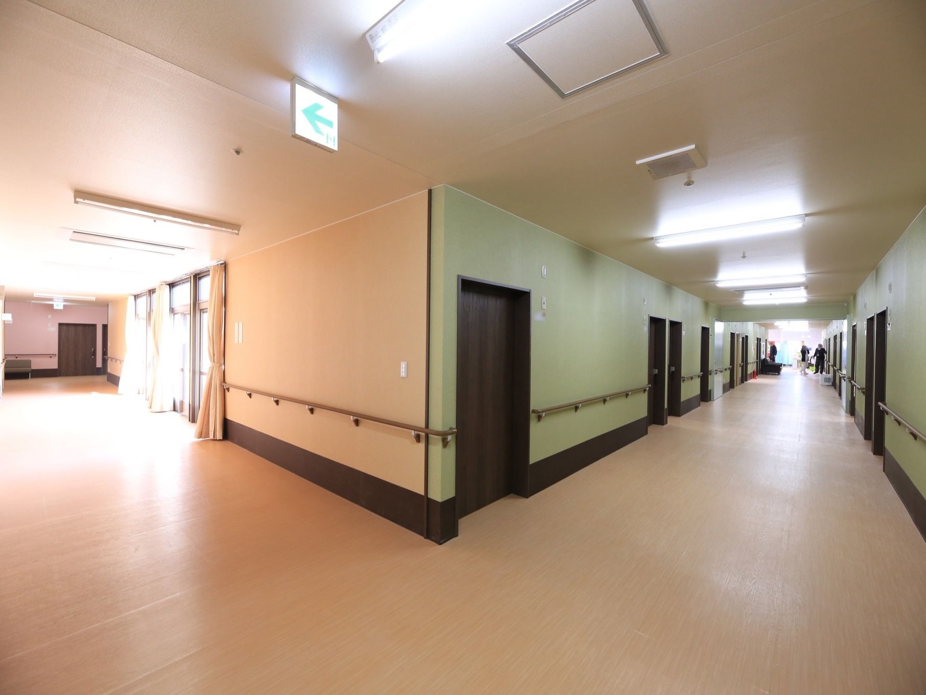 薄い色の床の広々とした廊下が二手に分かれている。いくつかの掃き出し窓があり、カーテンが掛けられている。