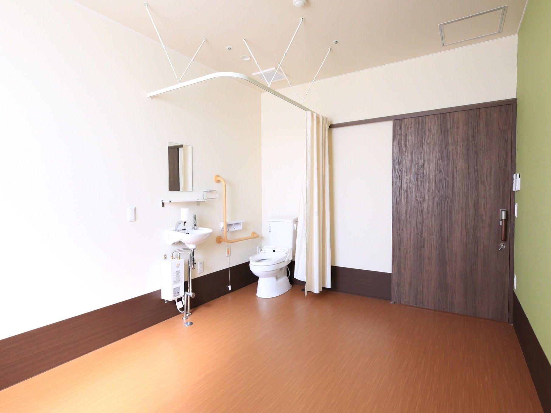 居室の入口は落ち着いた色の扉が設置されている。トイレと洗面台のスペースをカーテンレールが囲っている。