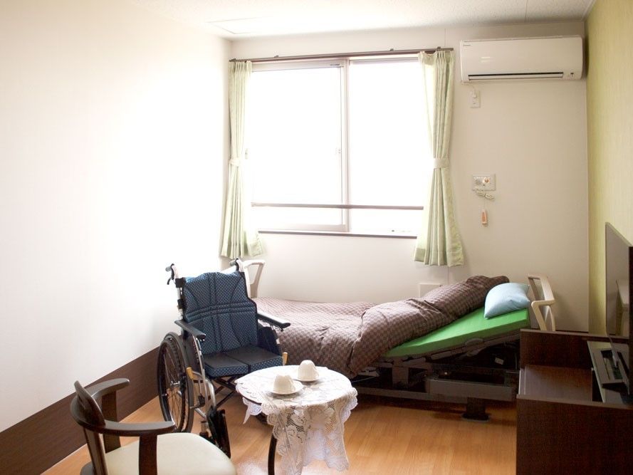 大きな窓のある明るい部屋である。介護用のベッド、エアコンが設置されていて、快適な生活を送ることができる。
