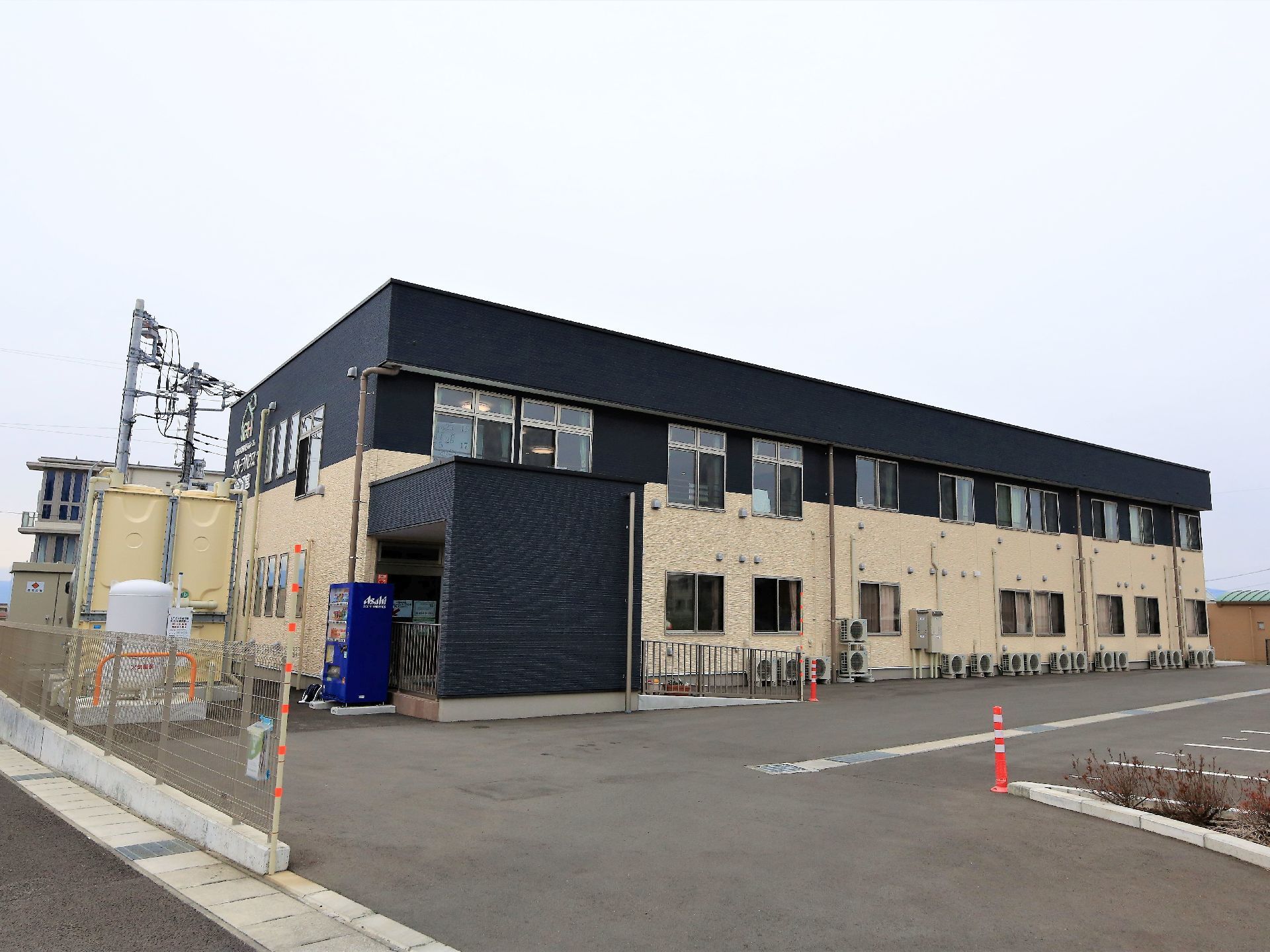 ツートンカラーの2階建ての施設外観である。建物脇には広々とした駐車場が設けられている。また玄関前にはスロープがついている。