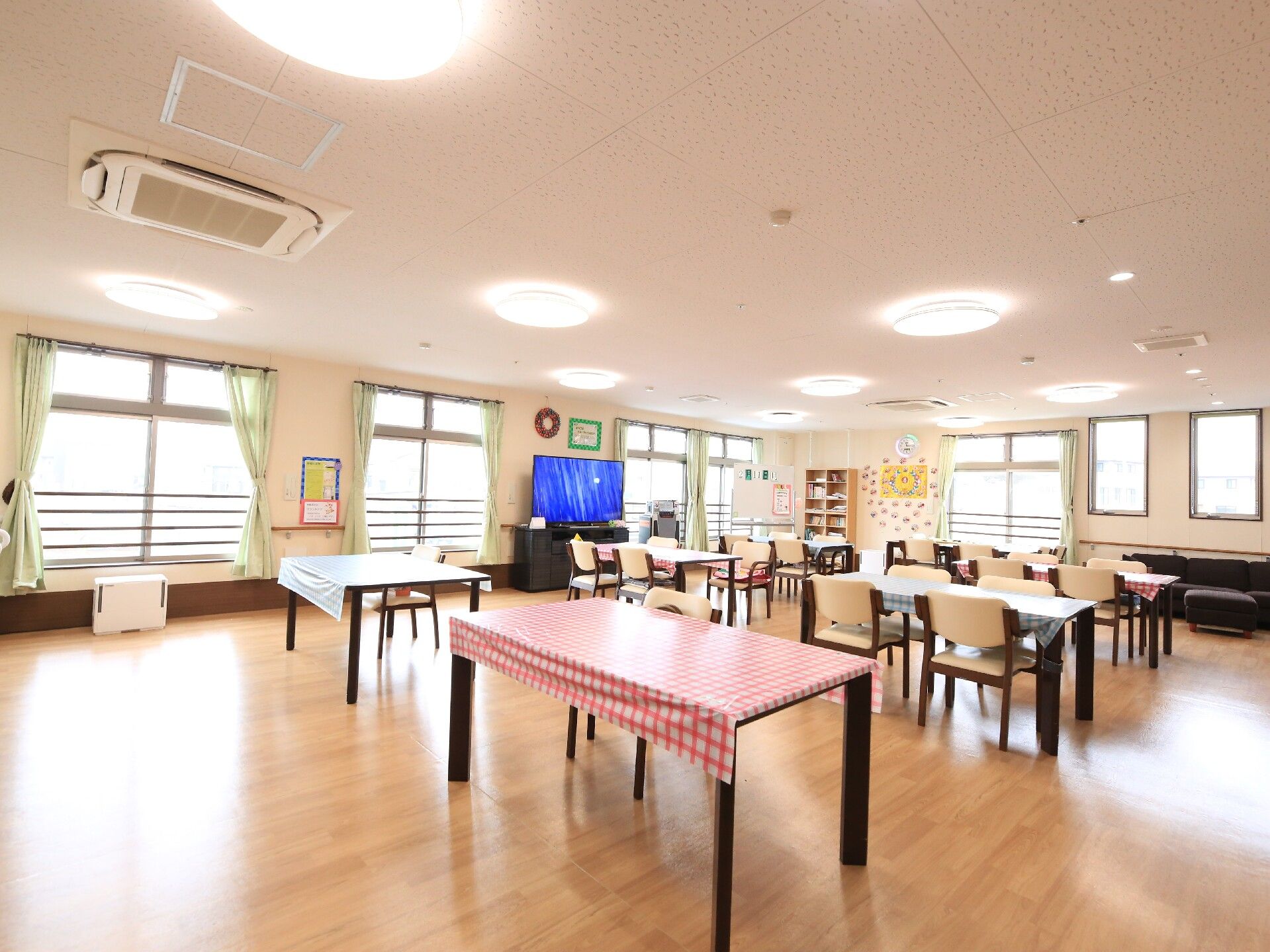 ソファとテレビが置かれ、チェックのクロスが掛けられたテーブルセットが並べられた食堂