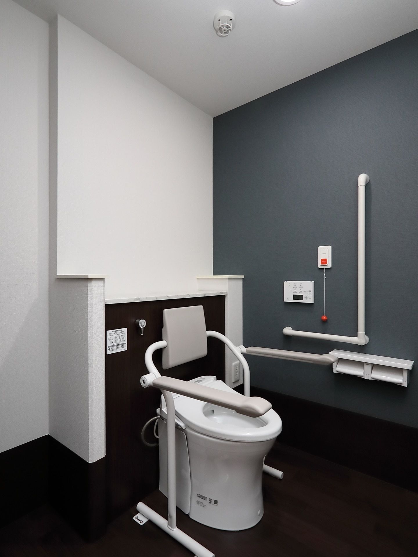 モノトーンの配色の洗練されたトイレの様子。お一人でも安心して利用できるよう、温水洗浄便座に手すり、呼出ボタンを設置している。