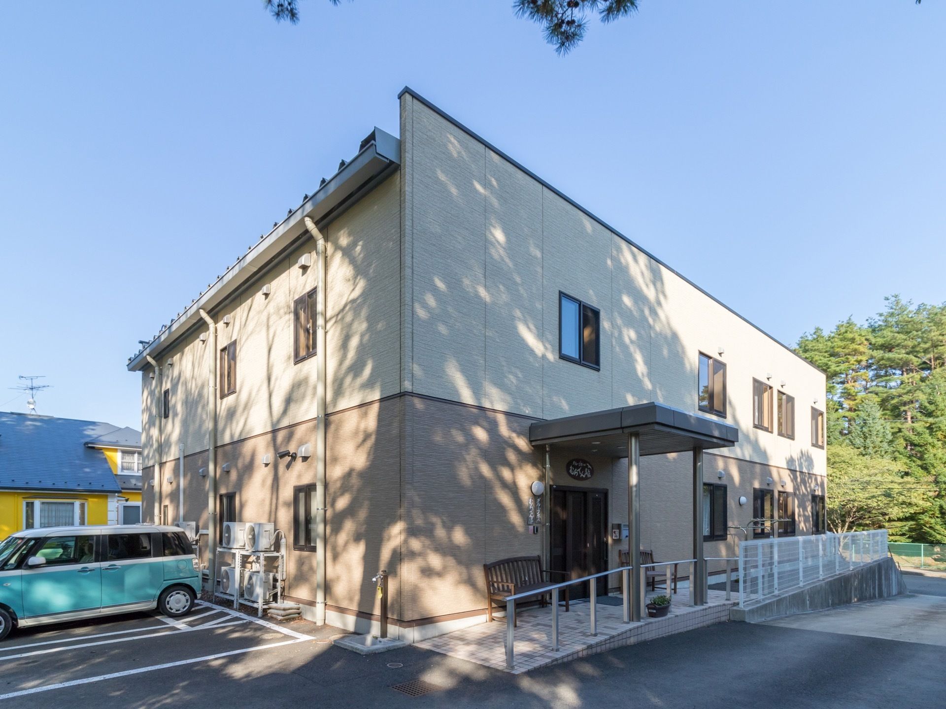 ベージュ色と茶色のツートンカラーの外観の２階建て建物である。建物横には、車を停めるスペースを設けている。