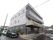 施設は落ち着いた色合いの３階建ての建物。建物に隣接して駐車場がある。車道と歩道は地面の色を変えて区別されている。