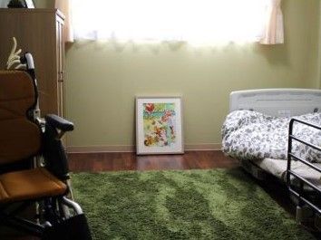 壁際には棚が設置され、近くには車椅子がある。窓の下には絵画が置かれている。ベッドには転落防止のための柵がついている。