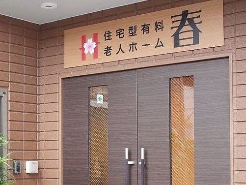 玄関は開き戸で、２枚両方開くと車椅子をご利用の方でも余裕を持って出入りすることができる。施設名の書かれた看板が玄関の上にある。