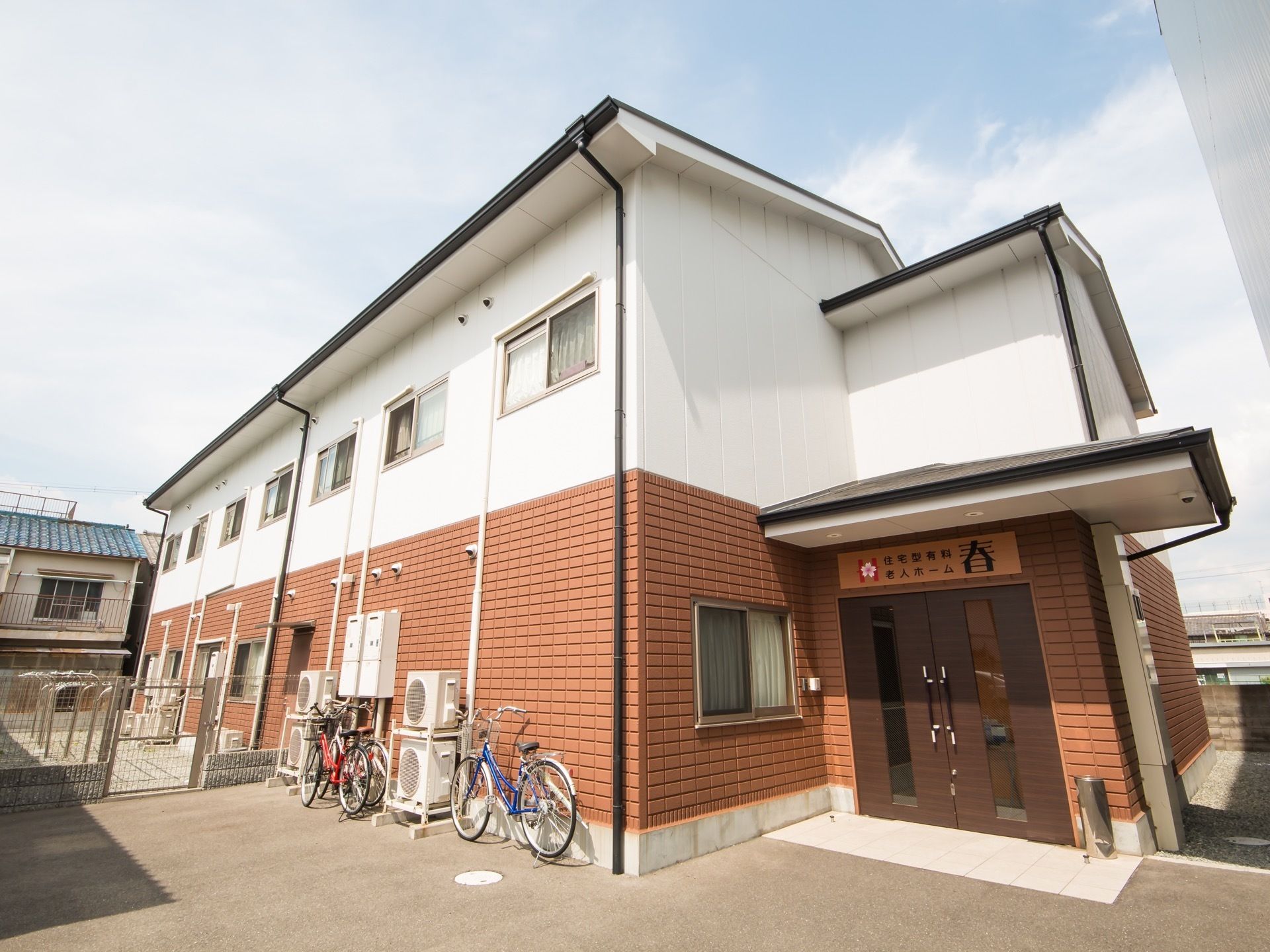 アットホームな雰囲気のある２階建ての建物である。エントランスの横に自転車が３台置かれている。周辺はアスファルトで整地されている。