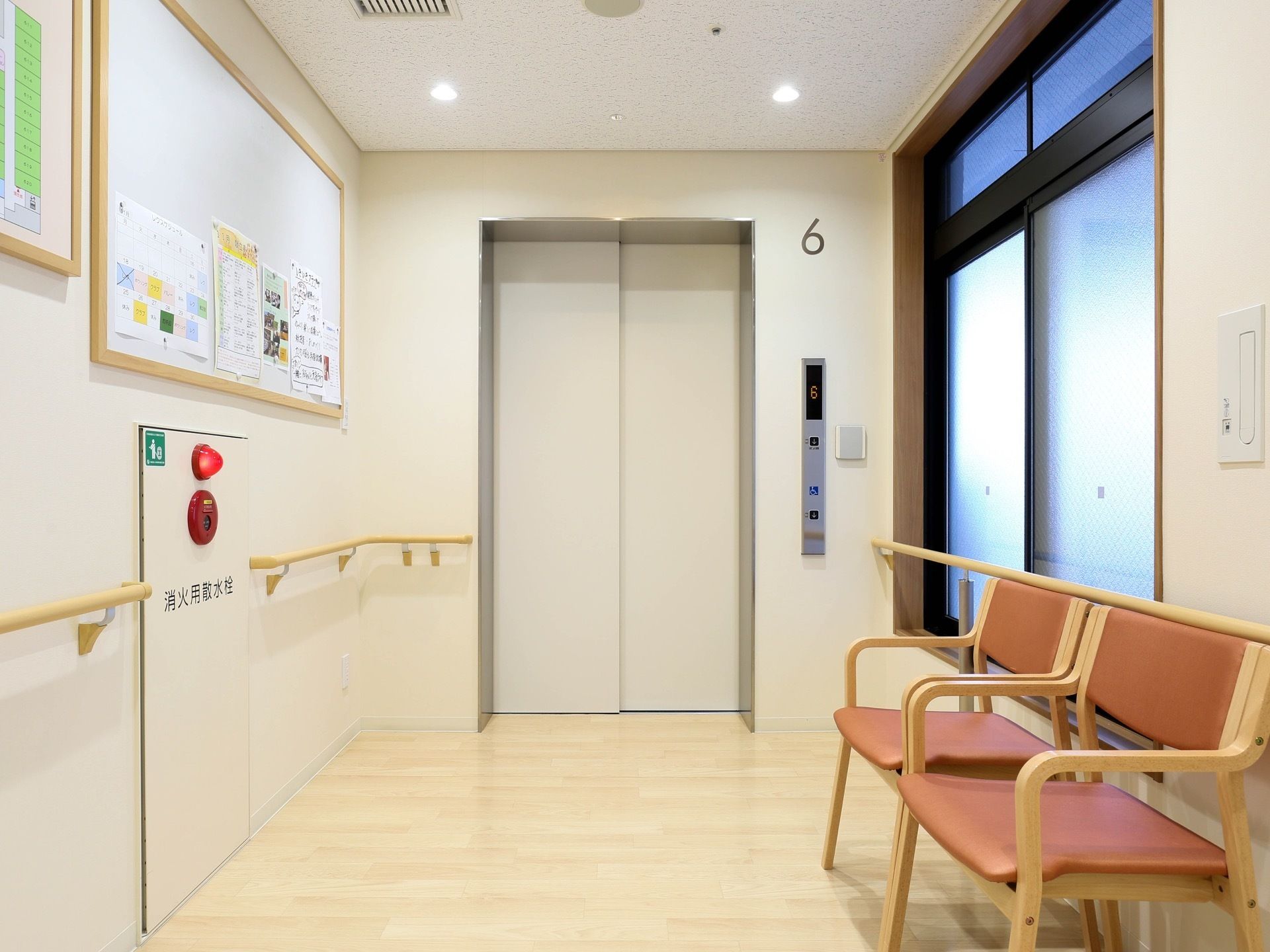 施設内に完備しているアイボリーのエレベーターである。壁に階数が示されている。窓側には、椅子が２脚置かれている。