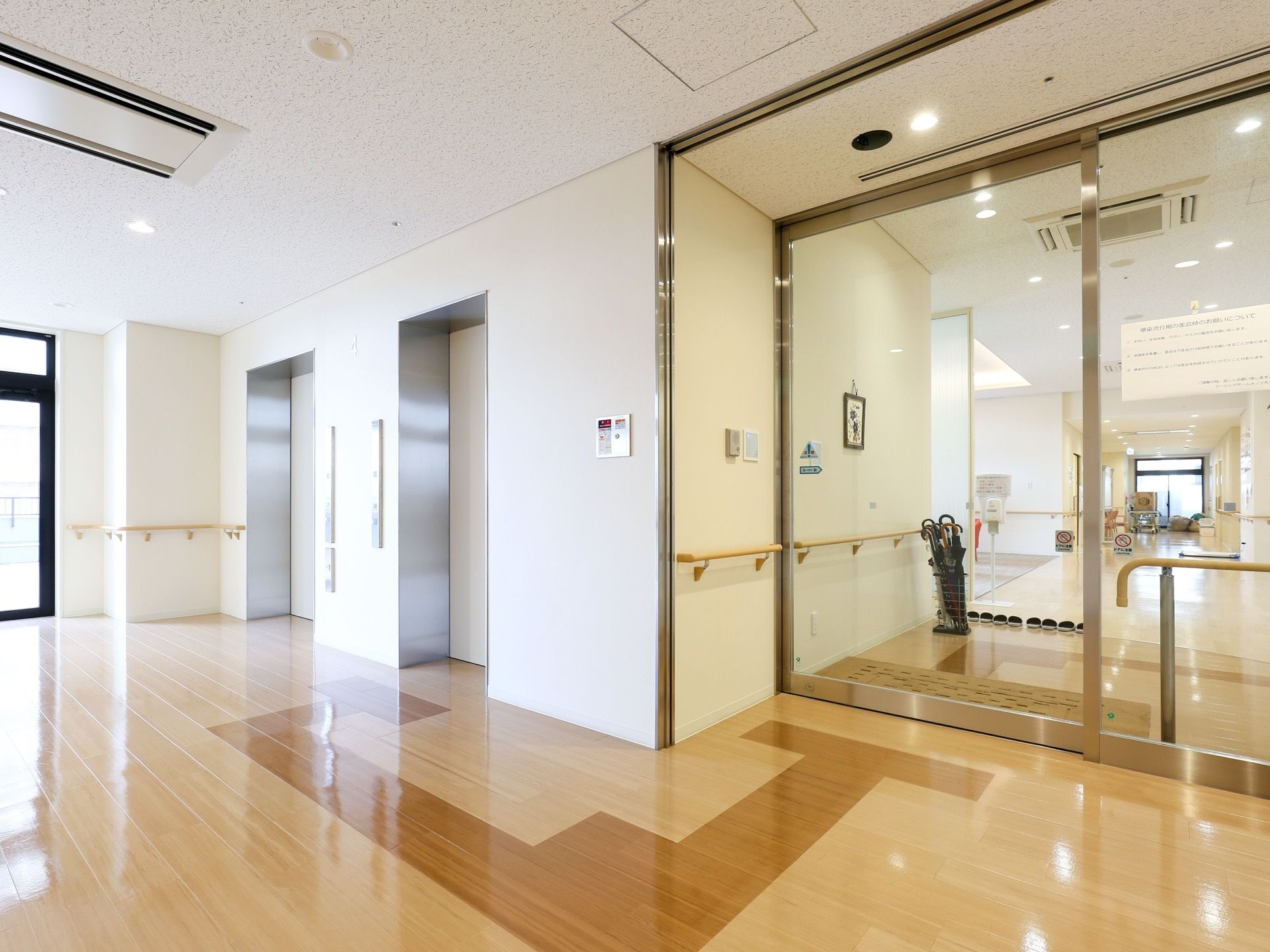 開放感ただよう通路である。エレベーターが２基完備されている。木目調のフローリング床。通路を示すカラーが施されている。