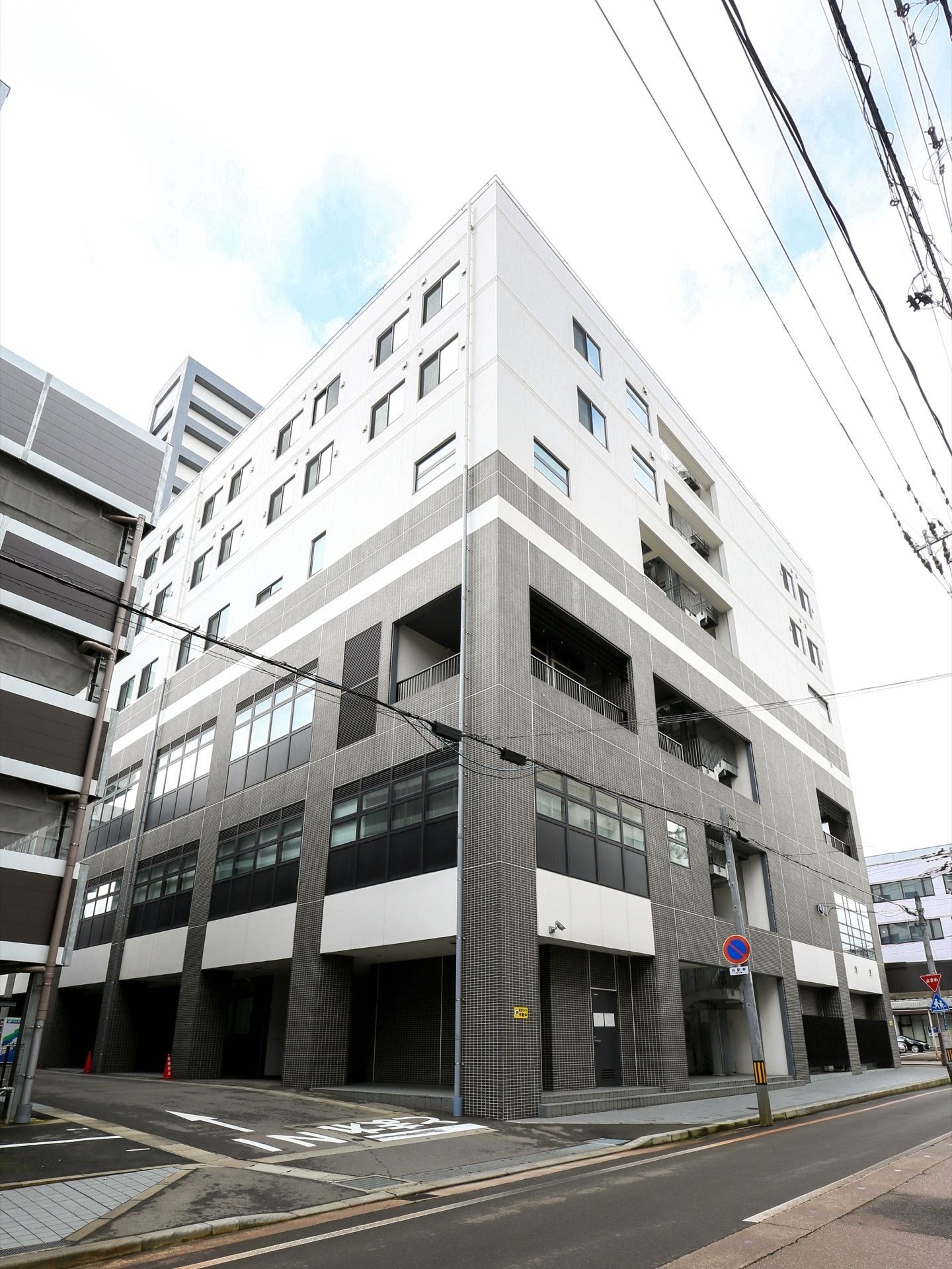 白とグレーのモダンな外観である。まわりは道路が走っている。中心市街地に位置する、介護付有料老人ホームである。