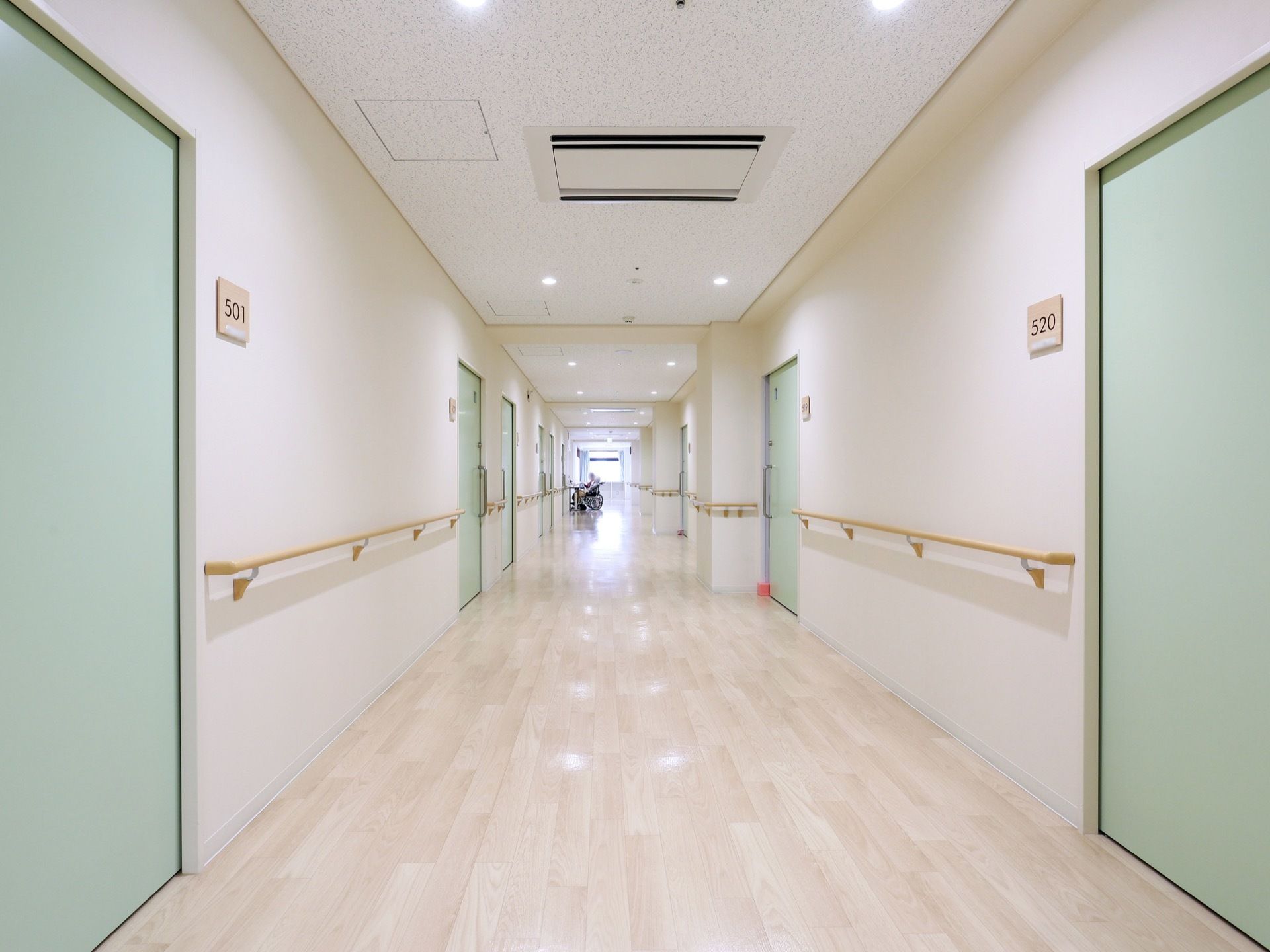 ホワイトを基調とした通路である。居室の扉は淡い、グリーンにあしらわれている。手すりも完備されている。