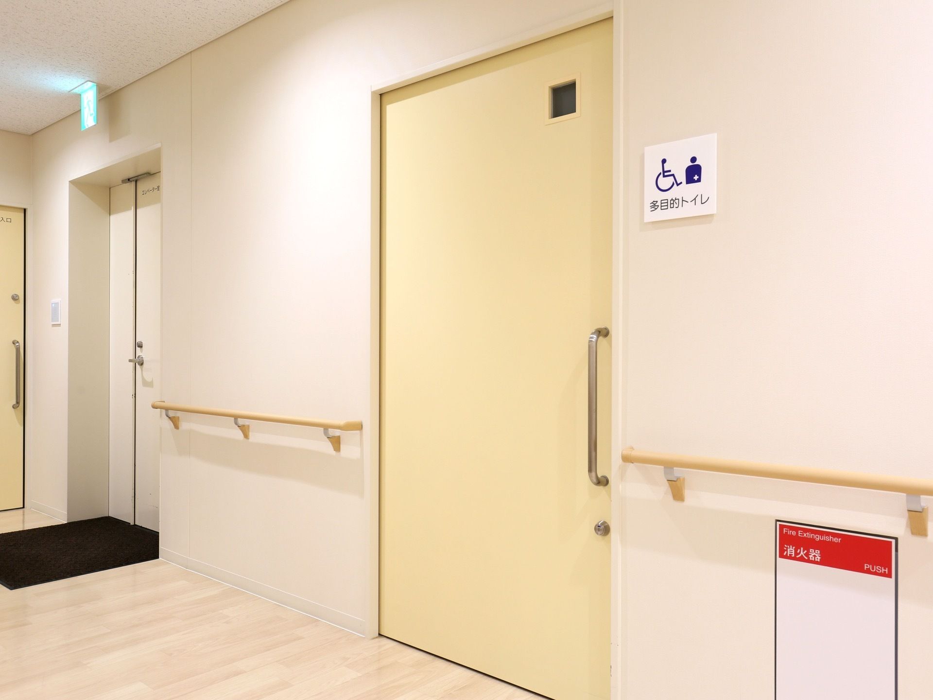 手すりが完備されている通路。消火器も備え付けられている。多目的トイレを示す、プレートが出入口に設置されている。