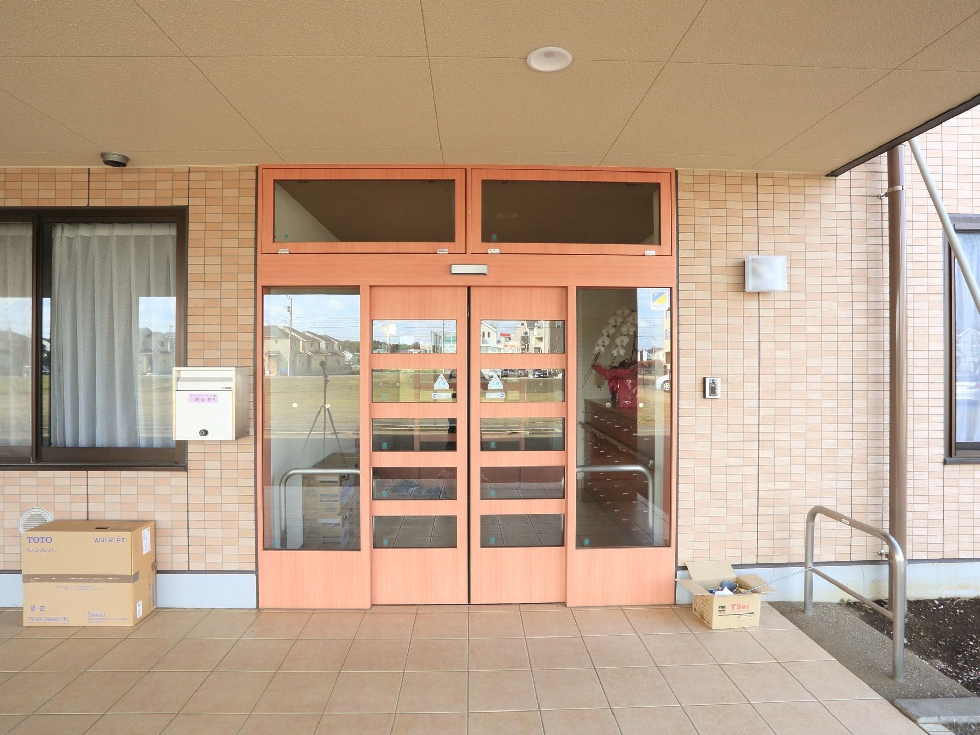 玄関の自動ドアは淡いオレンジ色で装飾が施されたものである。玄関前には屋根が備わったスペースが確保されている。