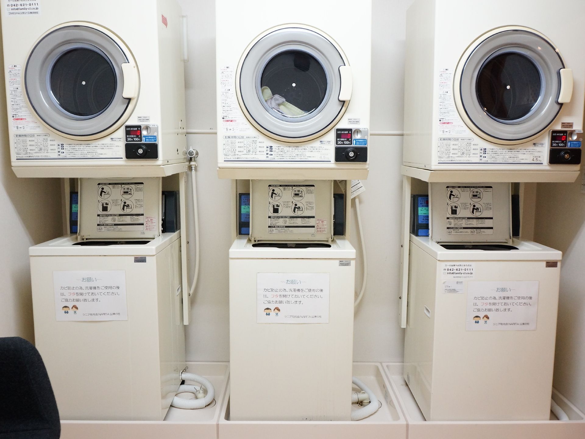 3台の洗濯機と乾燥機が並んでいる。一番右の洗濯機の横の壁に、縦方向の手摺が設置されていて、そちらに出入り口がある。