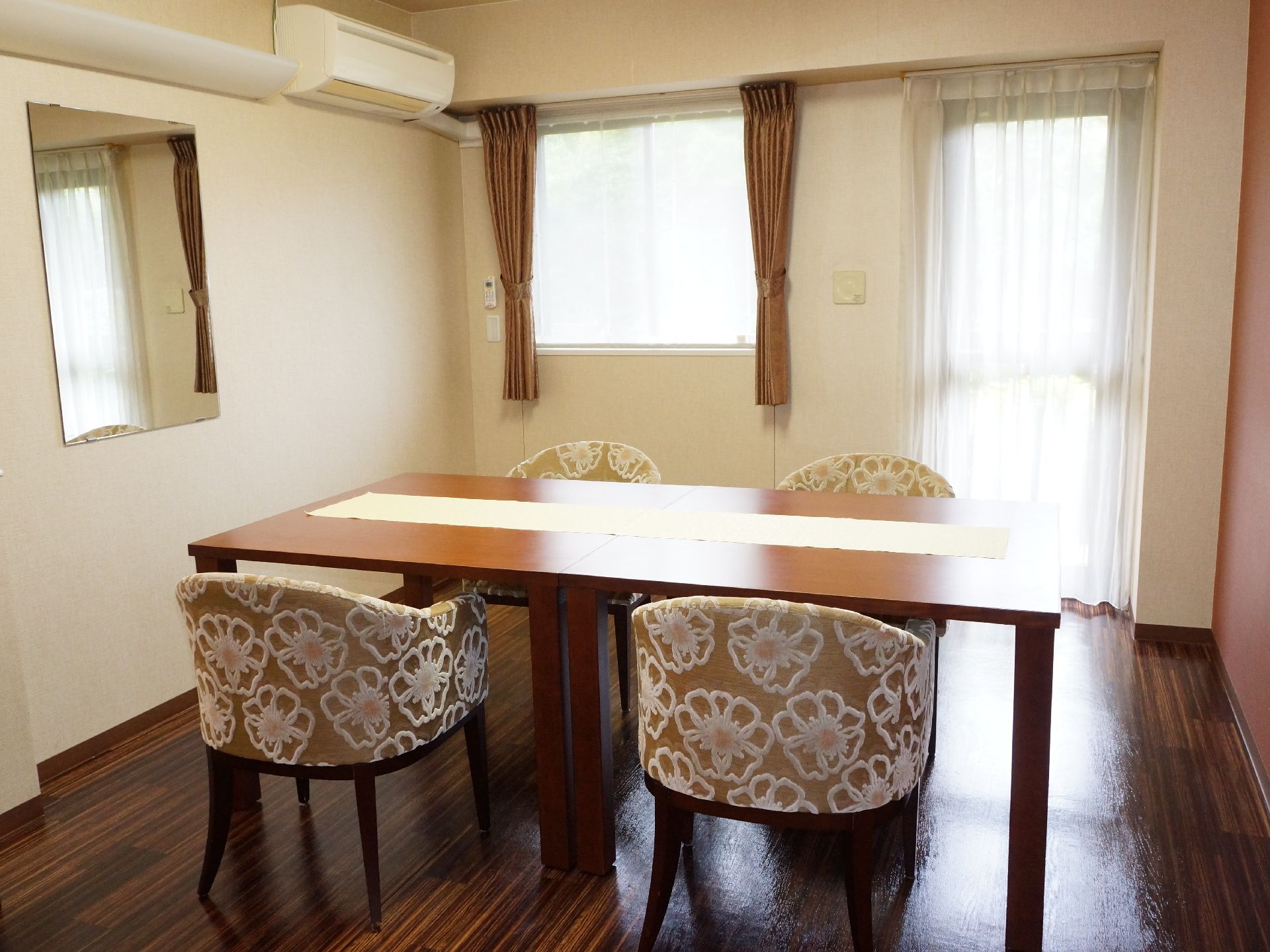 4人がけのテーブルが部屋の中央に置かれている。壁には鏡やライト、エアコンが設置されている。布張りの椅子がおしゃれである。