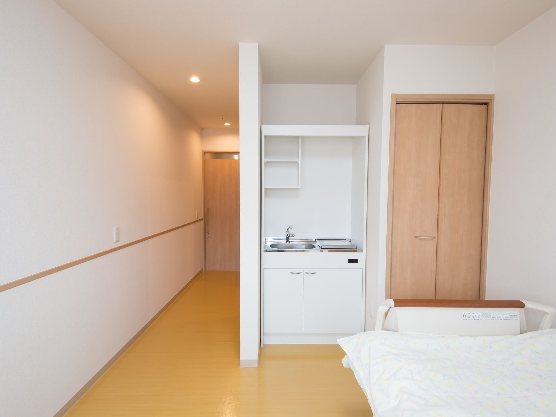 折れ戸の扉のクローゼットとキッチンがある。キッチンにはシンク下に扉がついた収納があり、壁に２段の収納が取りつけられている。