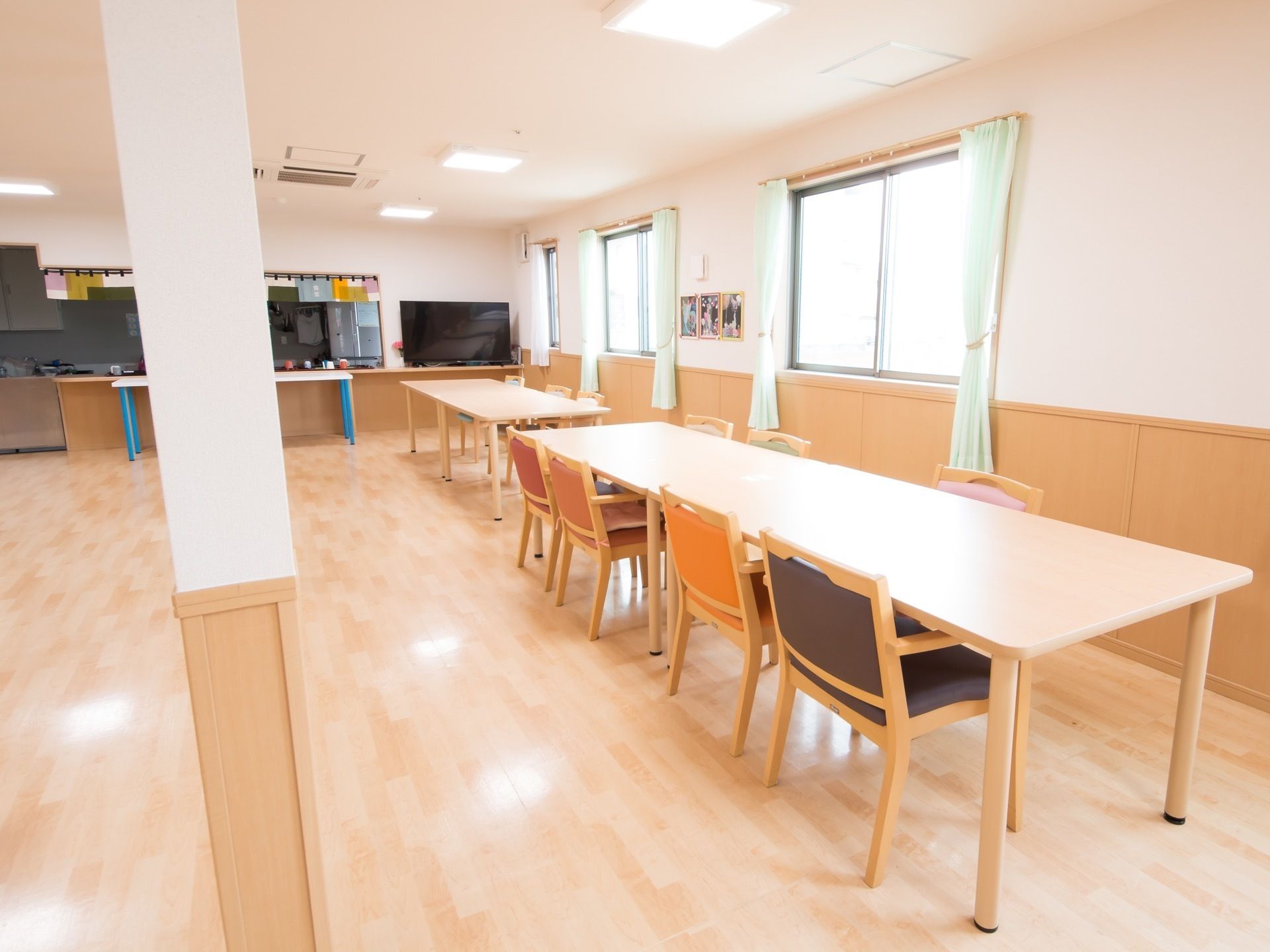 広々とした空間にダイニングテーブルと椅子がゆとりをもって配置されている。エメラルドグリーンのカーテンが掛けられた腰高窓がある。