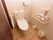 温水洗浄便座が採用されたトイレが設置されており、操作ボタンが壁に取り付けられている。壁にＬ字型の手すりがある。