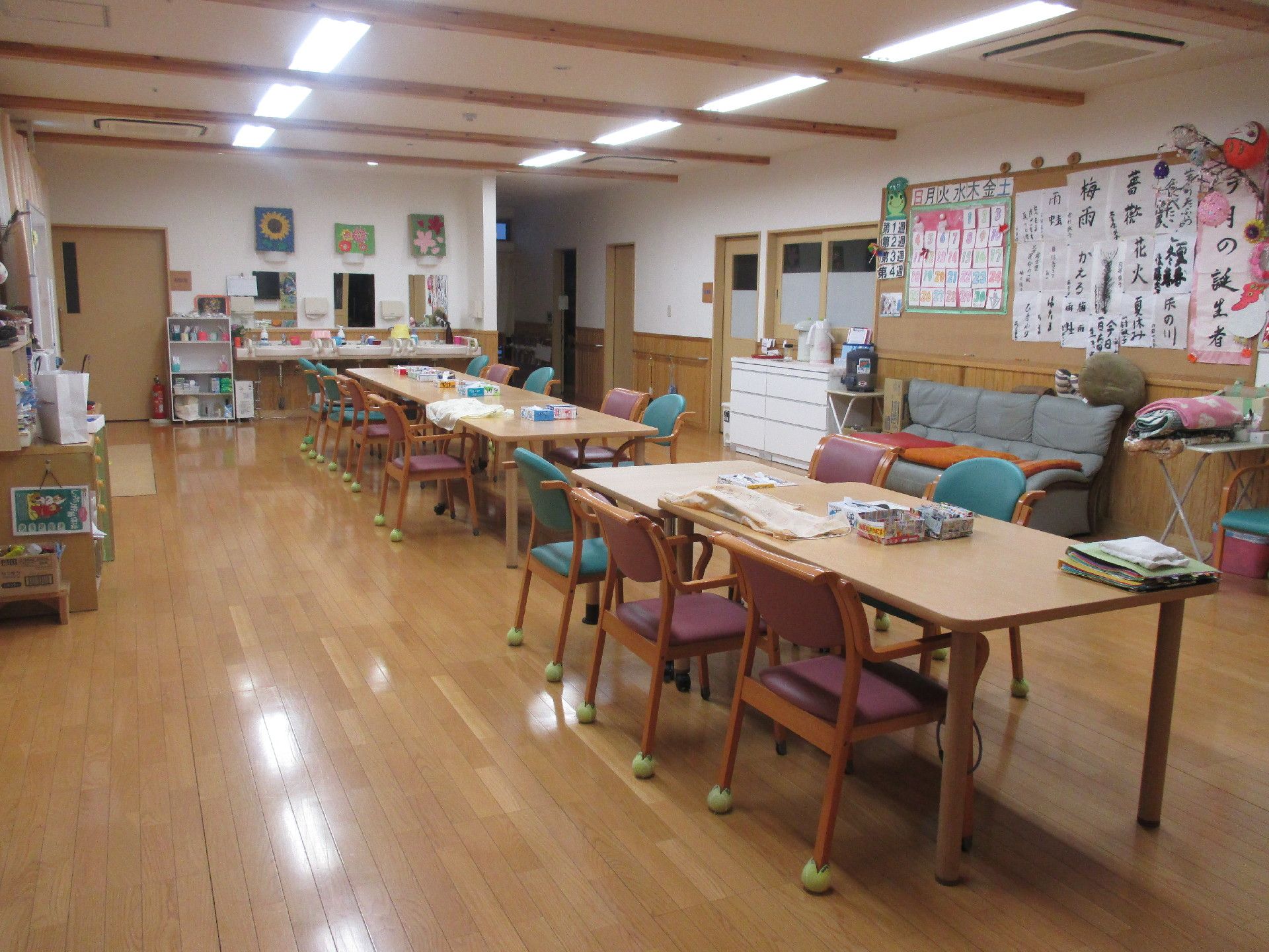 奥行きのある広々した一室。大きなテーブルが２つと複数の椅子が並べられている。壁側には３人掛けのソファがある。