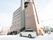 ベージュ色の外壁を持つ７階建ての施設である。建物の近くに車が３台停まっている。周囲に雪が積もっている。