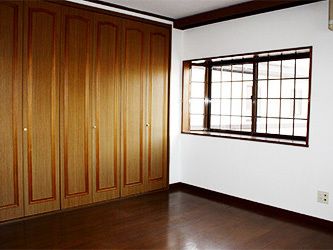 落ち着いた色合いのフローリングの居室。壁は白く、大きな出窓があり、もう一方の壁は全面がクローゼットになっている。