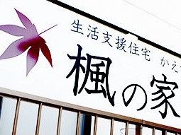 施設の看板写真。白い看板に黒い文字で書かれている。えんじ色のもみじのモチーフが和風でシックな雰囲気がある。
