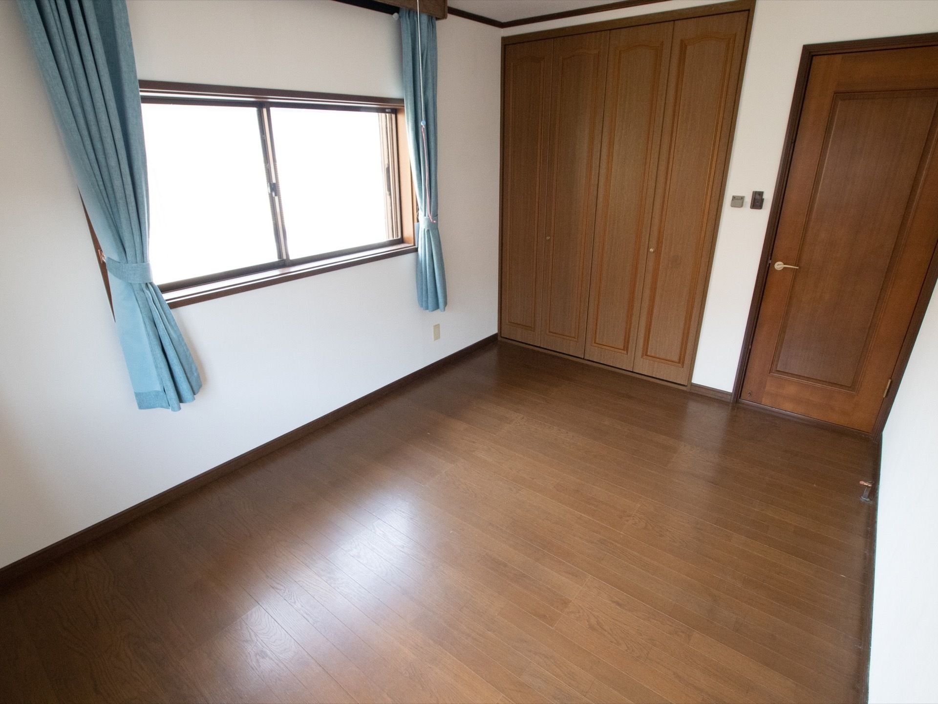 白い壁に木目調の床と扉で統一されている。窓の前には水色のカーテンが掛かっている。足元はバリアフリーになっている。