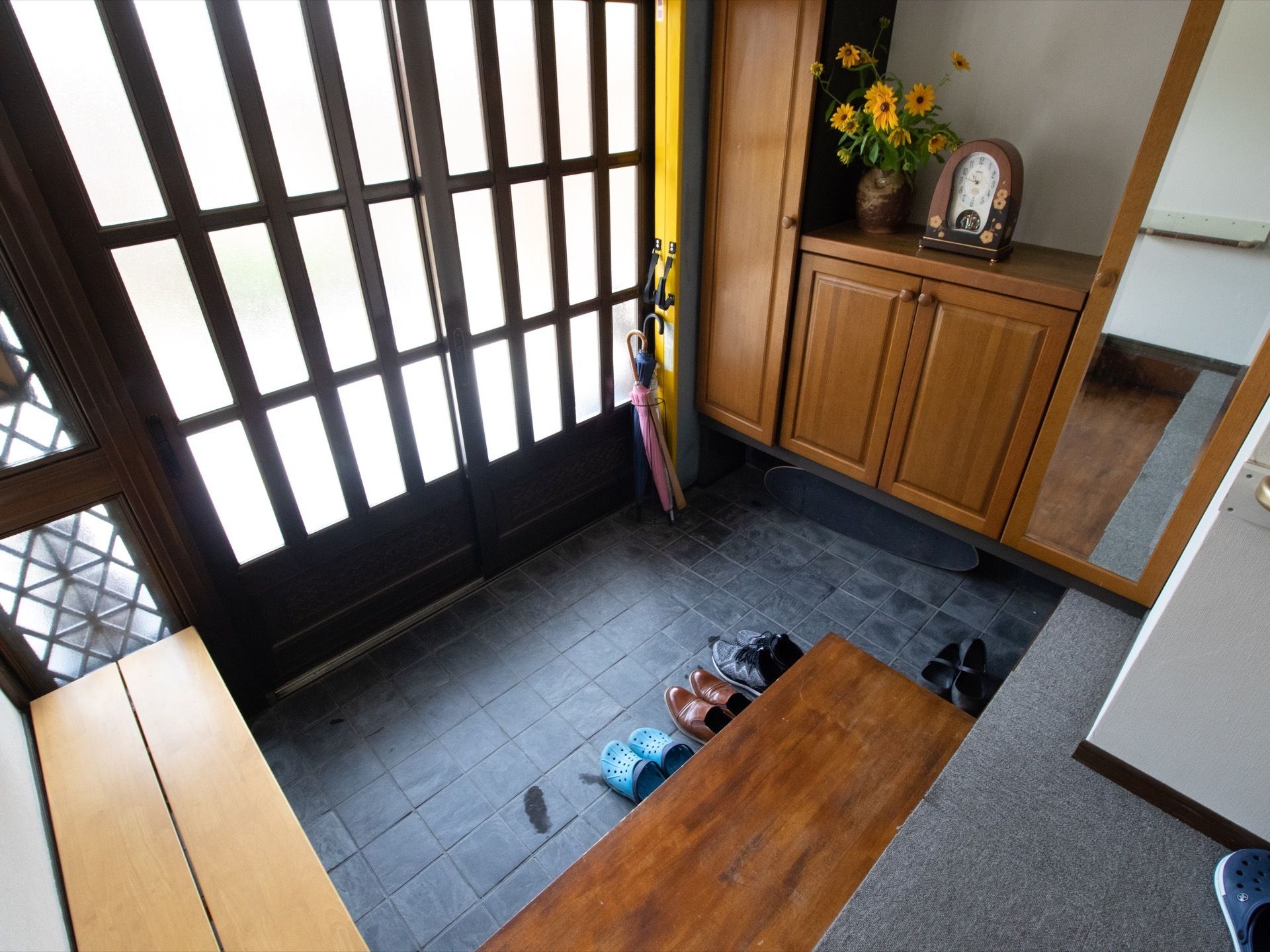 玄関扉は引戸式で曇りガラスになっているため明るい。壁側には扉のついた下駄箱がある。鏡と傘立ても置かれている。