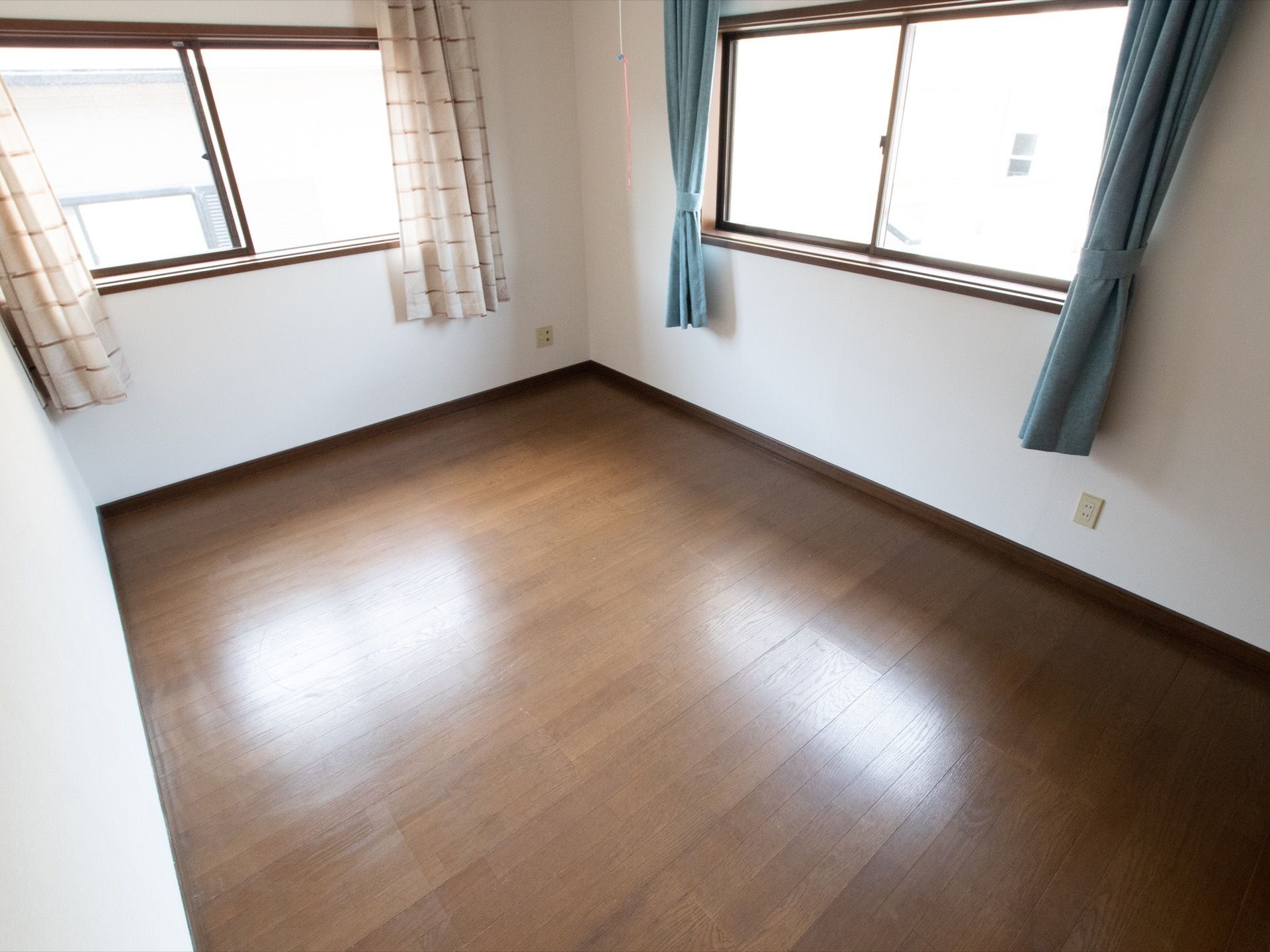 足元は木目調のフローリングで段差がない。窓は２ヵ所あり室内は明るい。緑とベージュ系のカーテンがかかっている。
