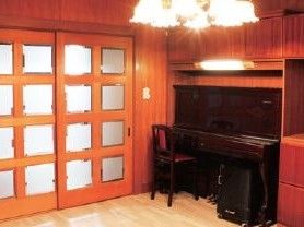 木目の壁とガラスの入った引き戸が落ち着いた印象の部屋である。豪華なシャンデリアにピアノも置かれている。