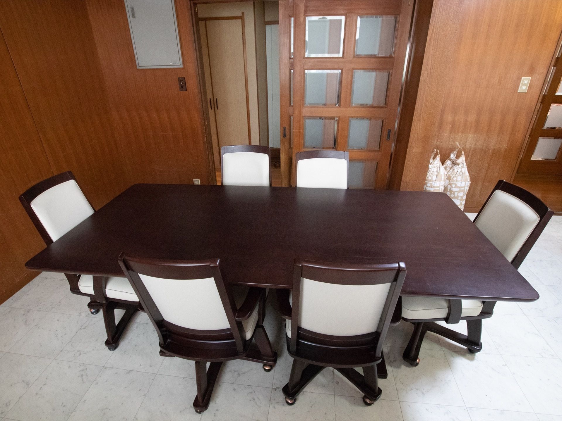部屋の中央に６人掛けのテーブルがあり、キャスター付きの椅子が６脚おかれている。廊下との境はガラス扉になっている。