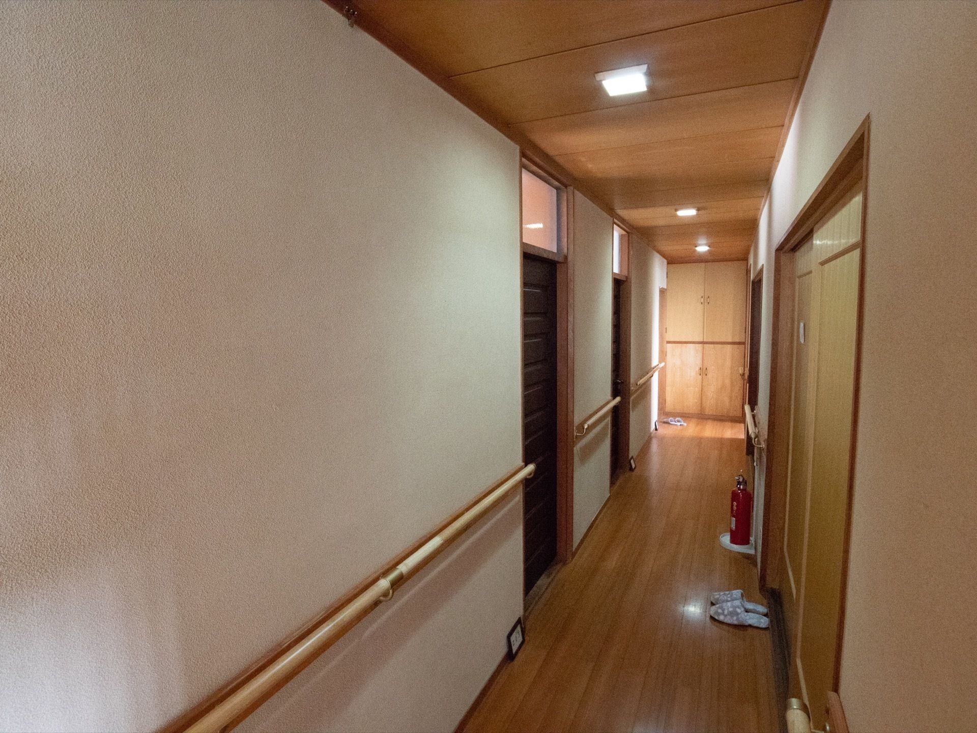 廊下には手すりが設置されている。突き当りには物入れがあり、廊下の中央には消火器が置かれている。所々にスリッパが置かれている。