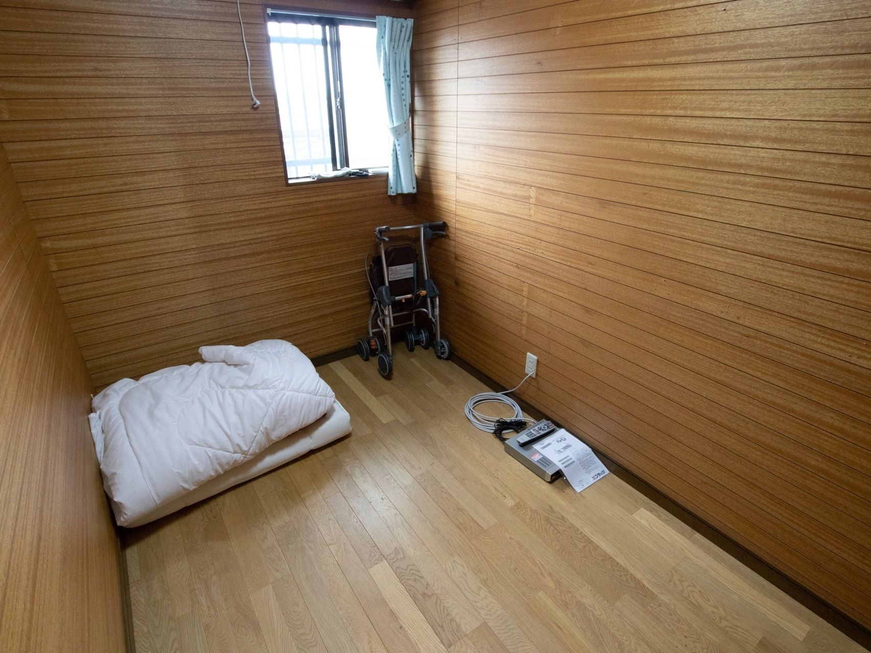 フローリングの居室である。布団が一組おかれている。木目調の壁紙が使われており、広く感じるような工夫が施されている。