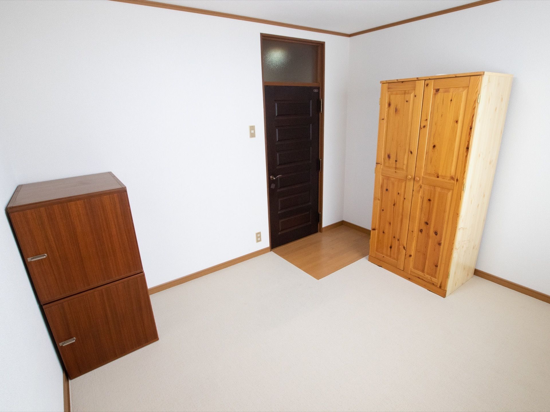 窓から光が差し込む明るい部屋である。白い壁や白い床が印象的である。洋服ダンスと整理ダンスが置かれている。