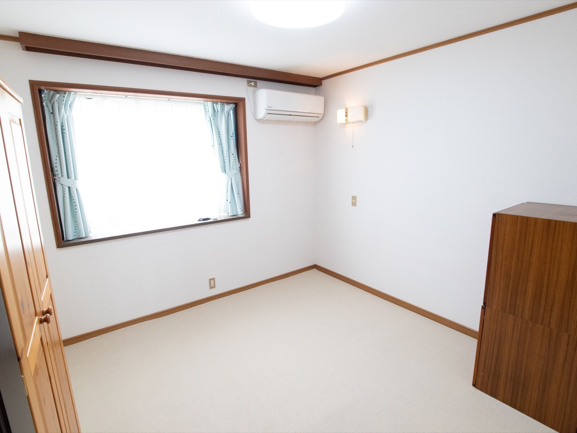 居室の壁は白く、建具はダークブラウンである。エアコンやクローゼットが設置されている。天井だけでなく壁にも照明器具が取り付けられている。