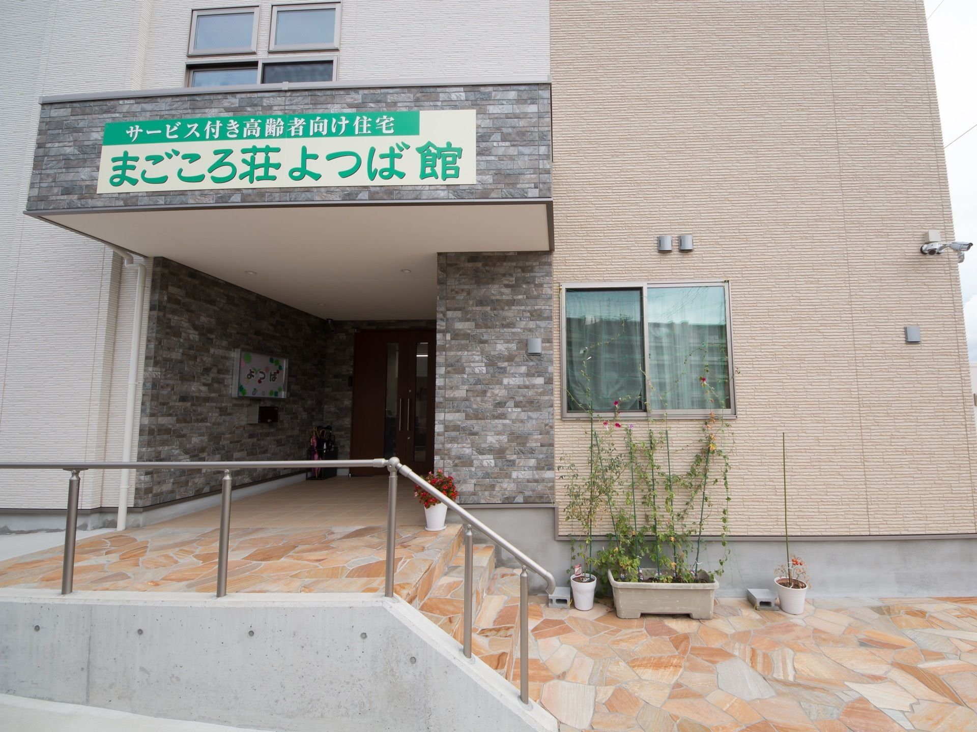 手前には階段があり、手すりが備えられている。ひさしには施設名が書かれており、ドアは少し奥のほうにある。